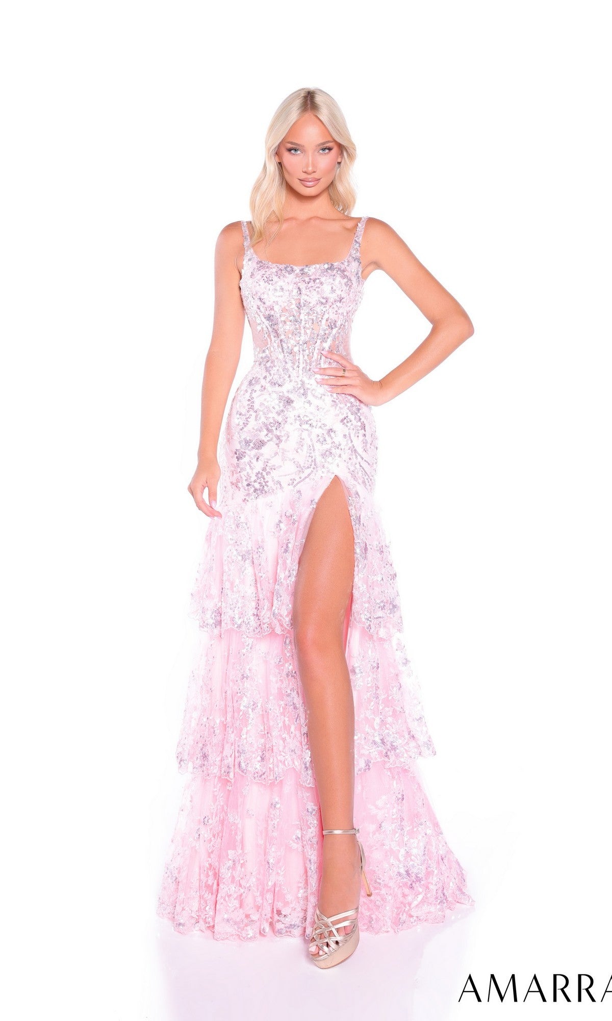 A woman stands against a white background wearing the Amarra 89377, a light pink long prom dress featuring sequins, embellishments, a tiered tulle skirt, and a high slit.